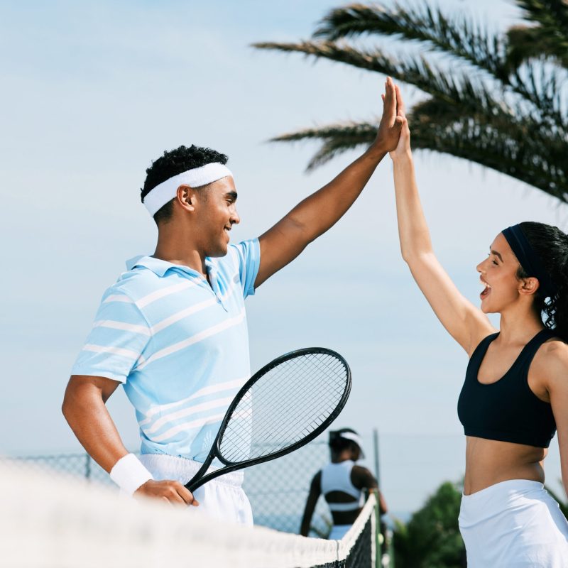 Muito bem. Foto de colegas de equipe de tênis comemorando com um "high five" durante uma partida de tênis.